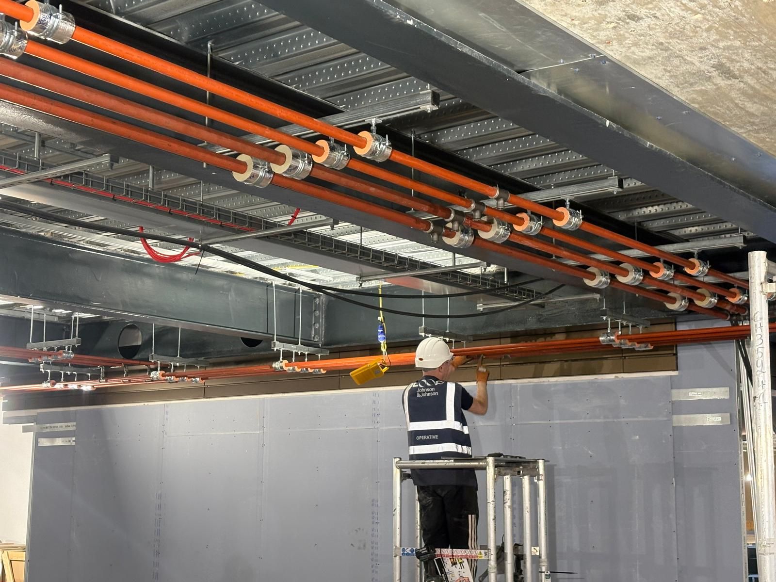 Operative installing bracketed copper pipework runs at high level